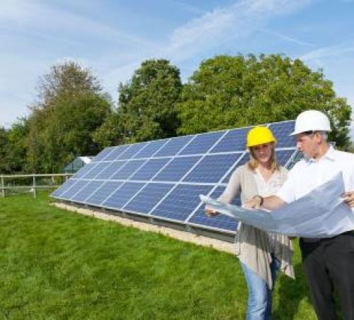 Man and a woman in hard hats looking at plans in front of a solar panel