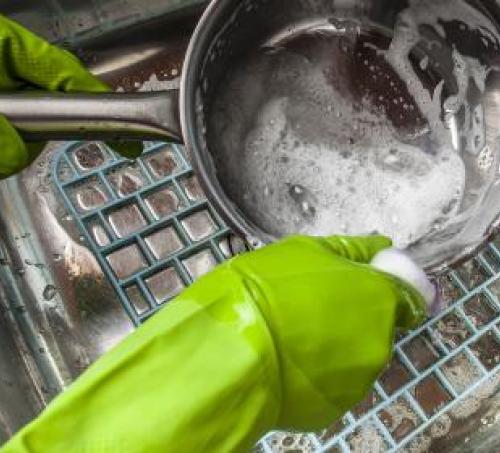 Gloved hands scrubbing a pot with soap