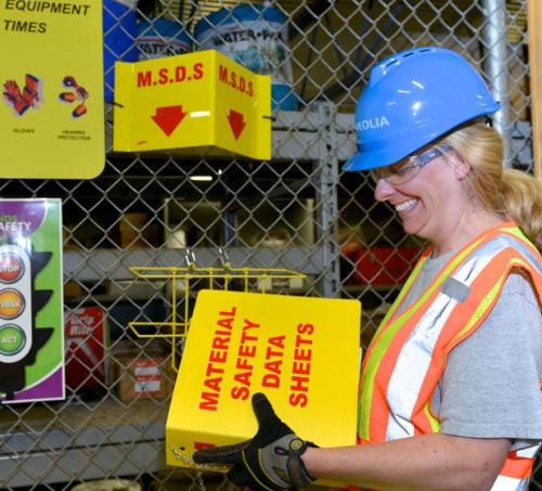 Woman at a warehouse holding a box labeled material safety data sheets