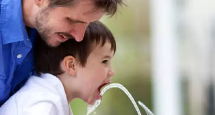 Father helping child drink from water fountain
